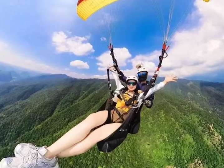 Tandem paragliding in Hui Zhou, China near Shenzhen and Guangzhou, flying above green mountain ridges under a bright blue sky.
